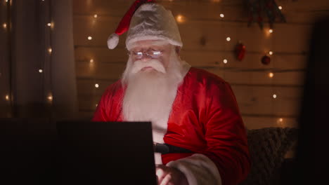Remote-work-of-Santa-Claus.-Online-shopping-and-ordering-gift-delivery.-Santa-is-working-at-home-with-a-laptop-on-Christmas-Eve.-Christmas-lights-and-decor